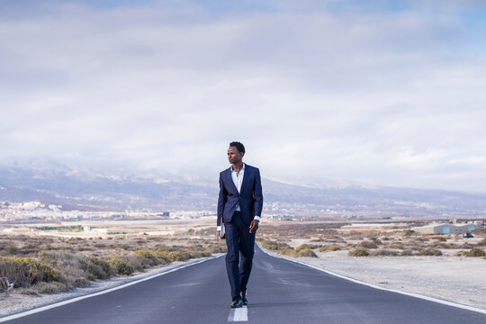 Spain, Tenerife, young businessman with laptop walking on road
