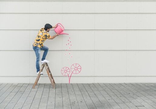 Digital composite of young man watering flower at a wall