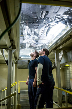 Two colleagues in factory checking underbody of a car