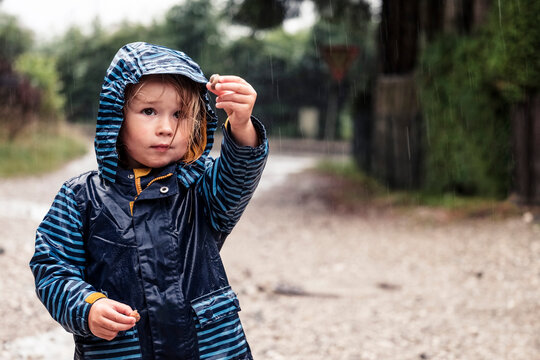 Portrait of little girl with snails in her hands standing in the rain