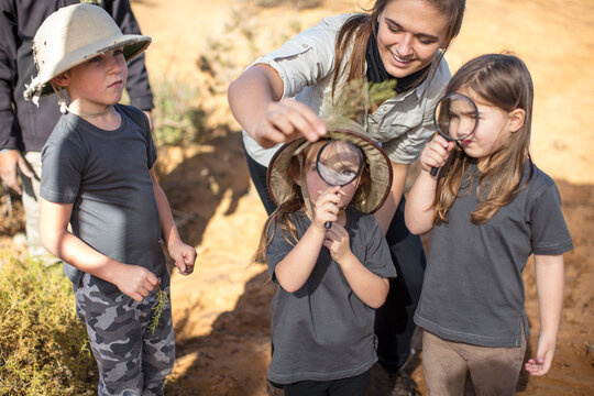 Children with teacher examining plant with magnifying glass