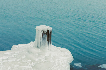 View of a frozen dock post with white foam on calm water during winter days