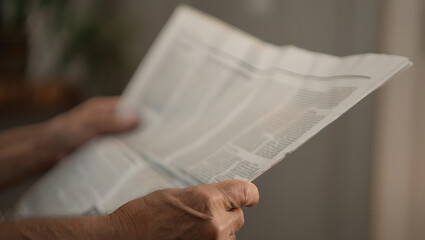 Naklejka premium Senior person's hands holding an open newspaper with blurred text.