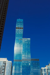 Modern skyscrapers rise high against a clear blue sky in an urban setting during daytime with sunlight reflecting off glass surfaces
