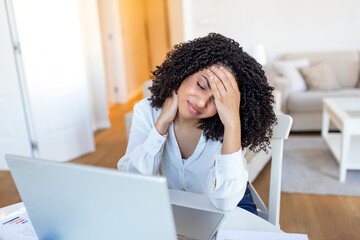 Obraz premium Headache at work. Migraine pain, People with body-muscles problem, Healthcare And Medicine concept. Attractive woman sitting at desk holding head and neck with hands while using her laptop at home.