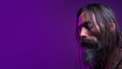 Moody portrait of mature man with beard, dramatic light expressing deep emotions and individuality. Creative male with long hair and beard. Smooth violet background. Banner template with copy space.