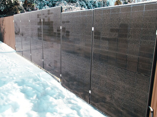 Modern solar panel array installed as a fence in a snowy backyard during winter.