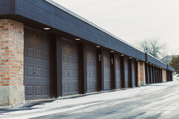 Storage units are lined up in a row showing gray doors with some snow on the ground in a location during winter