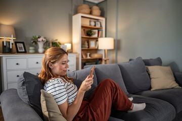 Woman relaxing at home checking smartphone on couch