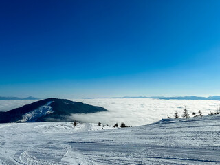 Clouds cover the landscape while snow rests on the mountains during a clear winter day in a ski resort