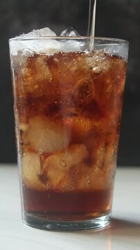 pour cola into a glass filled with ice cubes on black background. Vertical video