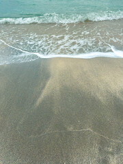 Waves rolling onto a sandy beach with light blue water during daylight hours