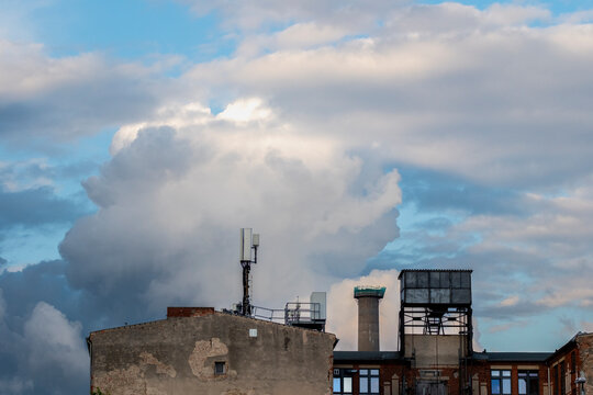 Industrial rooftop scene with weathered building chimney and antenna against towering clouds and open sky delivering minimal urban copy space background