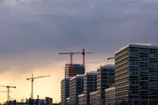 Dusk urban skyline with clustered buildings and active construction crane beneath layered clouds and open sky providing minimal copy space for city growth