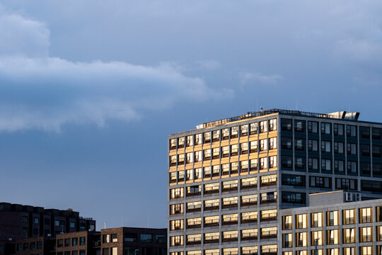 Sunlit office building facade with illuminated windows in modern urban city under soft clouds and wide sky giving minimal copy space for business themes