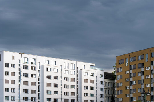 Modern residential apartment blocks with clean facade and window grid beneath dramatic clouds creating minimal sky copy space for urban city concept