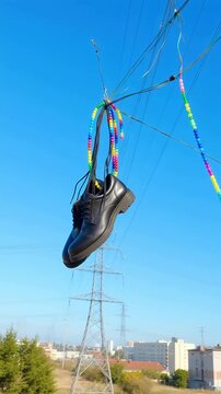 Black dress shoes dangling from power lines with colorful beaded strings against a clear blue sky