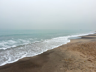 Ocean waves wash onto the shore with a cloudy sky in the background, captured during a quiet moment near the beach in the early morning