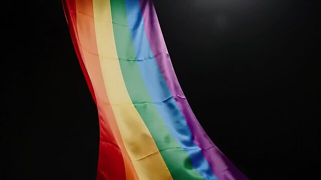 Rainbow flag waving against a dark background, symbolizing diversity and pride.