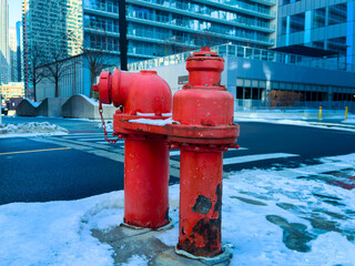 Red fire hydrants stand on a sidewalk covered in snow near modern buildings in an urban area during wintertime