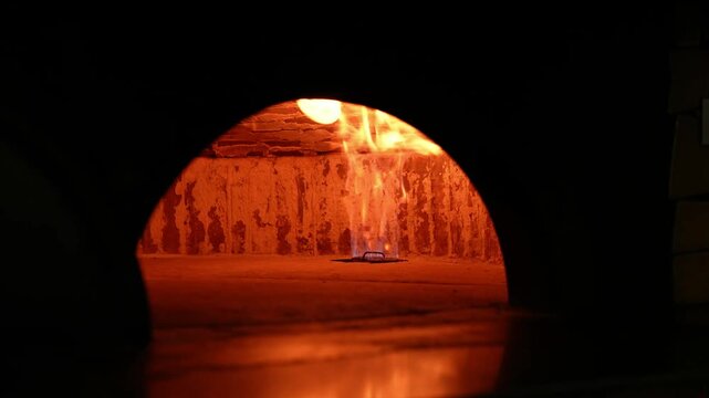 Fresh pizza baking in a wood-fired gas oven.
A close-up of a delicious pizza with olives and cheese, baked in a traditional professional oven, against the bright backdrop of gas flames.