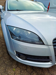 Silver car parked in a lot with close-up view of the front, showing details of the headlights and grill in a typical urban setting during daylight
