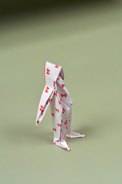 A side view of a white paper origami figure with small red bow prints standing on a smooth green surface under soft lighting