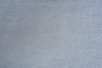 A close up full frame shot of a light blue denim fabric surface showing the detailed diagonal weave...