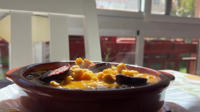 Steaming hot tripe and chickpea stew with blood sausage in a rustic earthenware bowl on a restaurant table