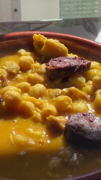 Delicious homemade tripe and chickpea stew with slices of blood sausage steaming in a clay pot. A classic Spanish comforting dish