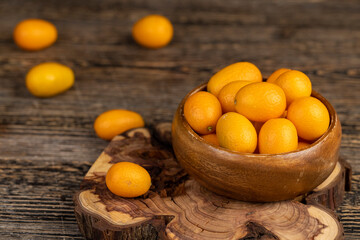 small orange fruits of juicy fresh and fragrant kumquat on a black wooden table, oval kumquat fruit scattered on a black table made of pine wood