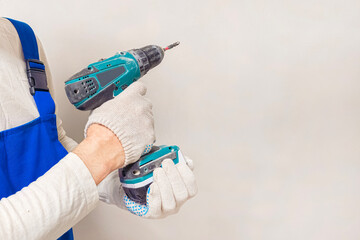 A man is holding a power drill, wearing gloves.