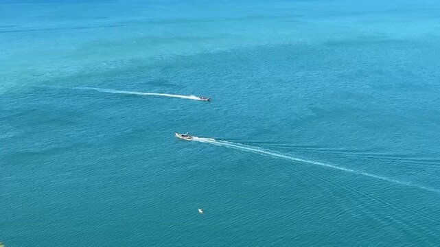 A stunning high-angle shot capturing two motorboats gliding across the calm, crystal-clear turquoise waters of a tropical ocean.