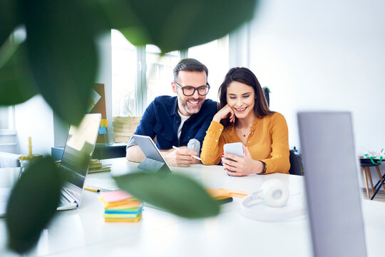 Two colleagues working together on tablet and smartphone in office