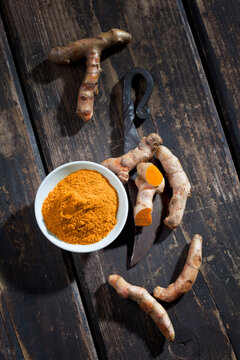 Whole and sliced turmeric, bowl of curcuma and an old knife on dark wood