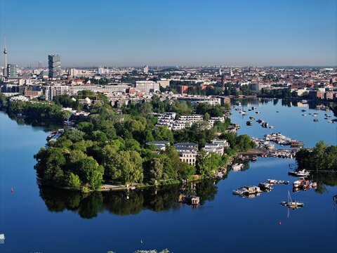 Aerial view of a vibrant green island community surrounded by calm waters, reflecting the city skyline with the iconic TV Tower, Berlin, Berlin, Germany.