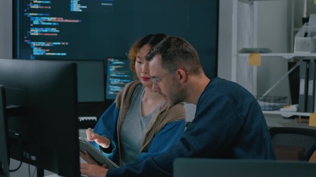 Focused diverse software engineers and AI developers working on code on computer screens in a dark office. Concept of machine learning, digital transformation, and future technology innovation.