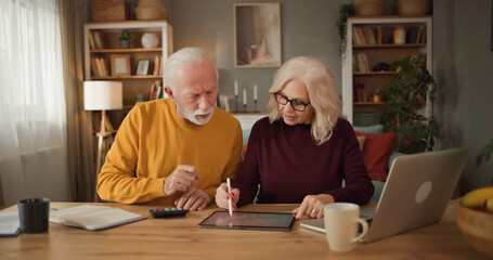 Older couple engages in a discussion about life insurance plans at home. They use a tablet and...