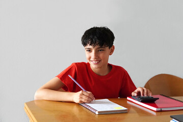 Young student in a red t-shirt working happily at his desk, learning with enthusiasm