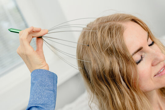 Closeup photo of young blonde woman using scalp massaging brush for hair growth. Scalp massage with wire head massager on woman&rsquo;s hair, eyes closed