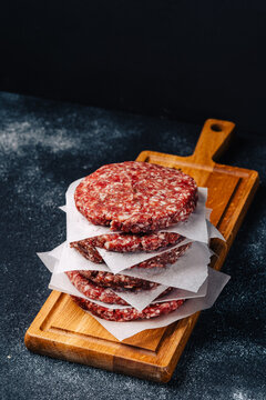 Fresh burger patties stacked on a wooden cutting board