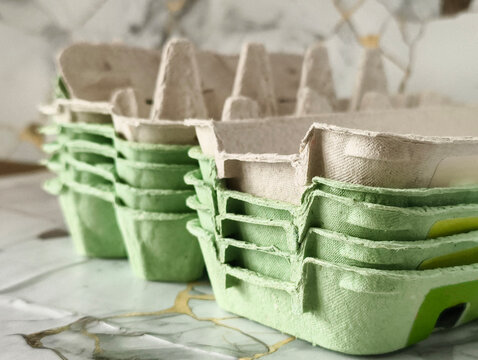 Stacked green and beige paper egg cartons on marble background, eco-friendly packaging concept.