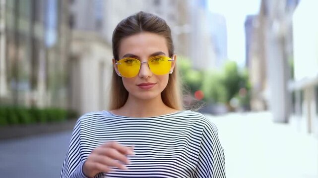 Confident young woman in stylish yellow sunglasses poses on a city street. Embracing urban fashion and self-expression in a vibrant environment