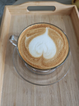 Top view of hot latte coffee cup with heart milk foam shape on wooden tray for romantic valentine morning breakfast in verticle shot concept