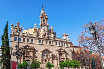 Obraz premium Baroque facade of historic Iglesia de los Santos Juanes in Valencia, Spain. Ornate sculptures and a clock tower rise above the bustling Plaza del Mercado near the central market