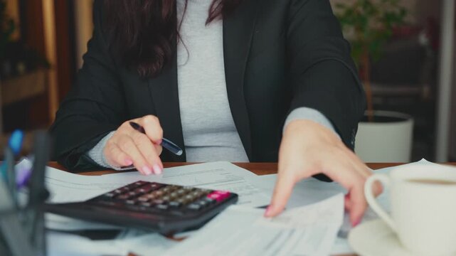 Close-up hands accountant working at office desk using calculator planning corporate budget. Stressed woman taking notes checking utility bills taxes bank account balance, calculating expenses indoors