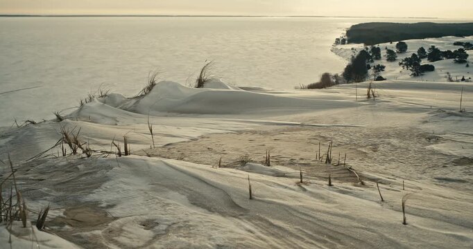 Winter view of the Dead Dunes at Nida on the Curonian Spit, Lithuania, covered in snow with a frozen Baltic Sea backdrop. Coastal landscape, cold weather, and serene mood