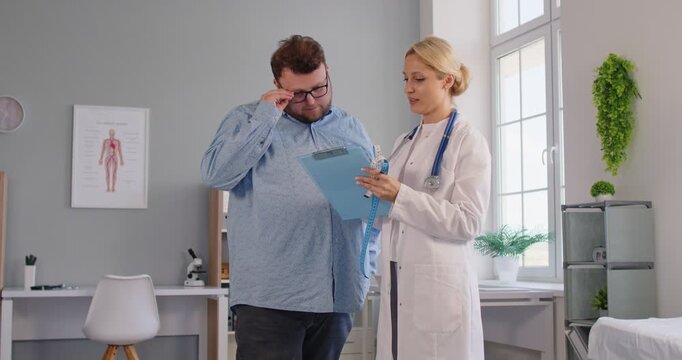 Doctor reviews results with fat overweight man patient. In healthcare consultation, they review the report on a clipboard and a discussion on next steps in medical clinic during exam.