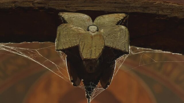 Ethereal wooden angel hanging beneath beam with faded paint and spiderwebs