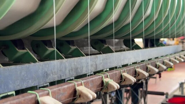 Multiple rotating bobbins collect fine threads simultaneously along a mechanized line, ensuring stable output during large scale silk production. Textile production.